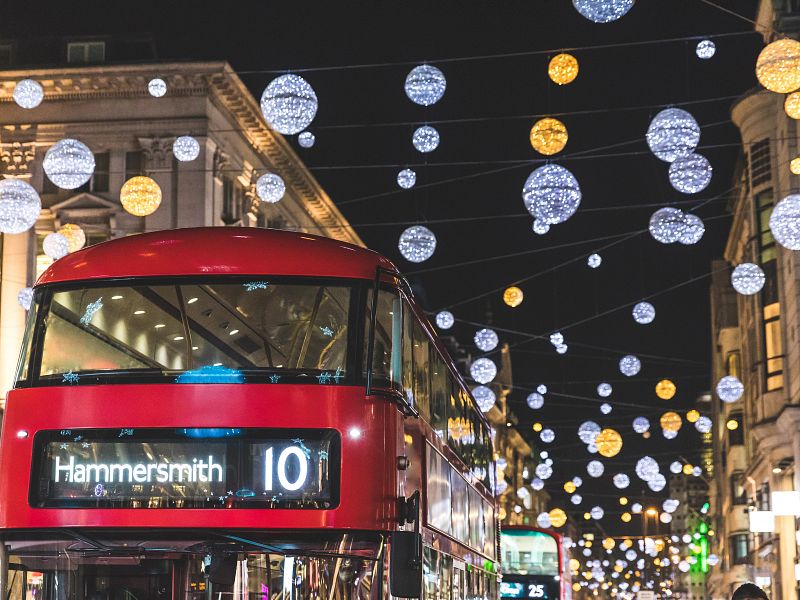 Red double-decker bus beneath glittering holiday light orbs in London