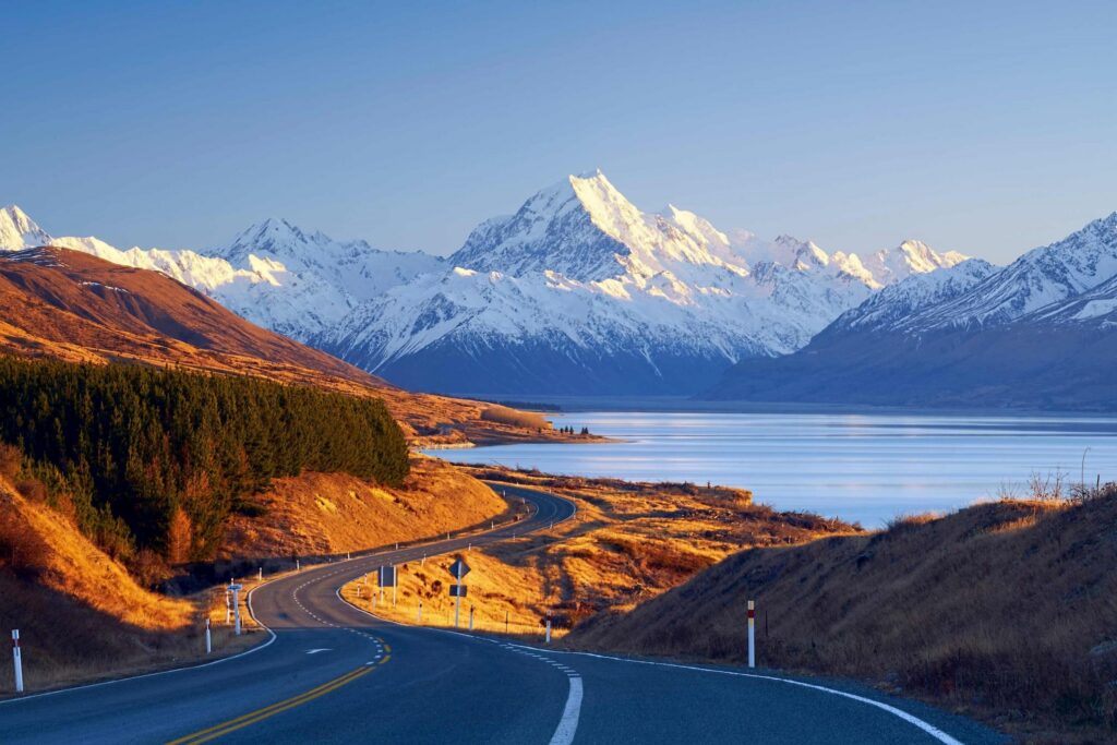 Snow-capped Aoraki/Mount Cook rises above Lake Pukaki and a winding road in New Zealand