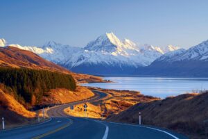 Snow-capped Aoraki/Mount Cook rises above Lake Pukaki and a winding road in New Zealand